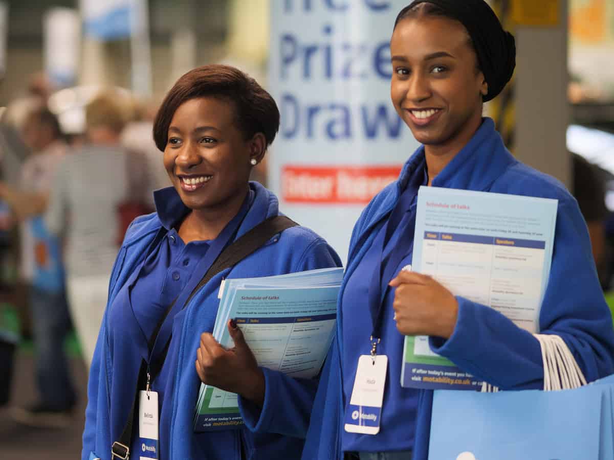 Two smiling event staff members holding brochures