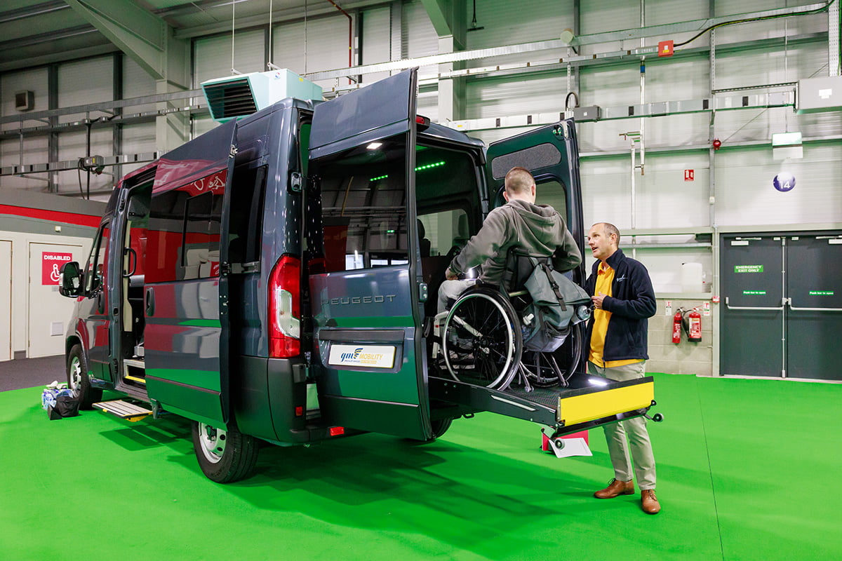 A person in a wheelchair using a lift to enter the back of a large van