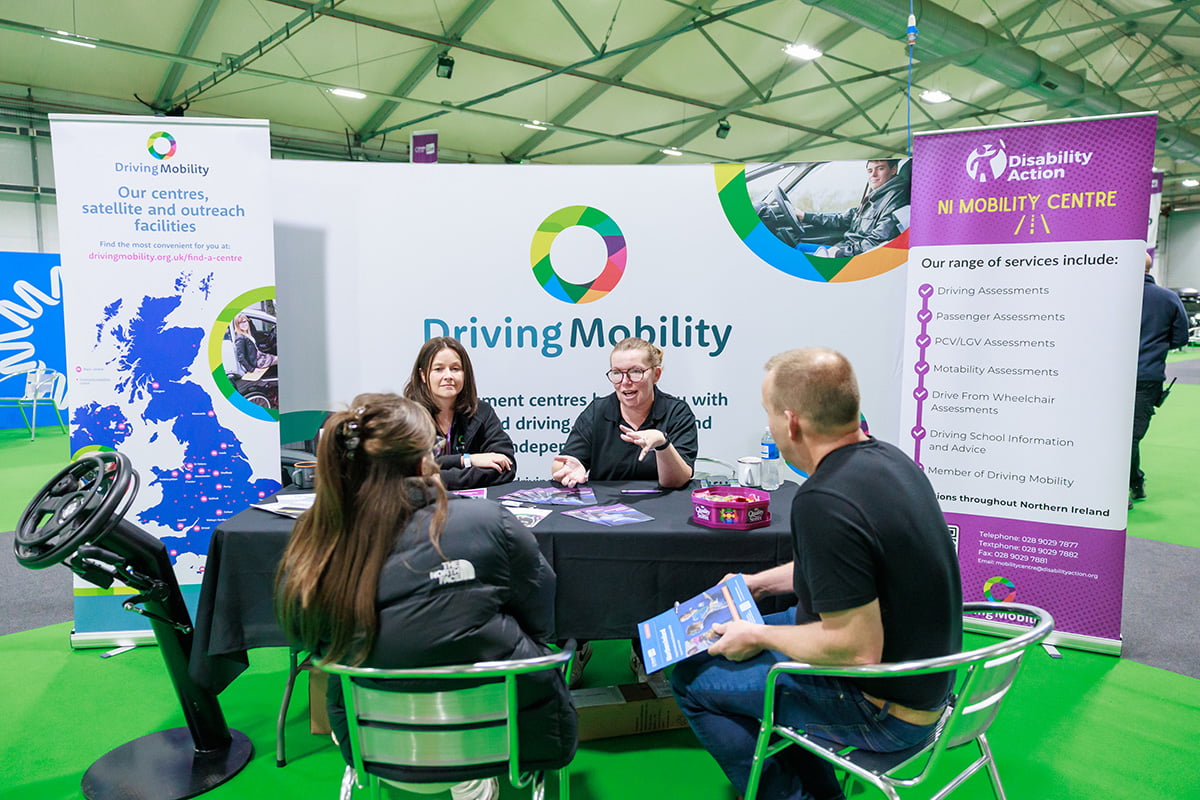 Staff at a Driving Mobility table speaking with two visitors at an exhibition
