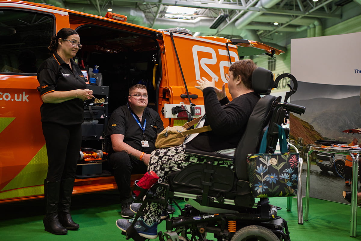A person in a wheelchair talking to RAC roadside assistance staff next to an orange RAC van