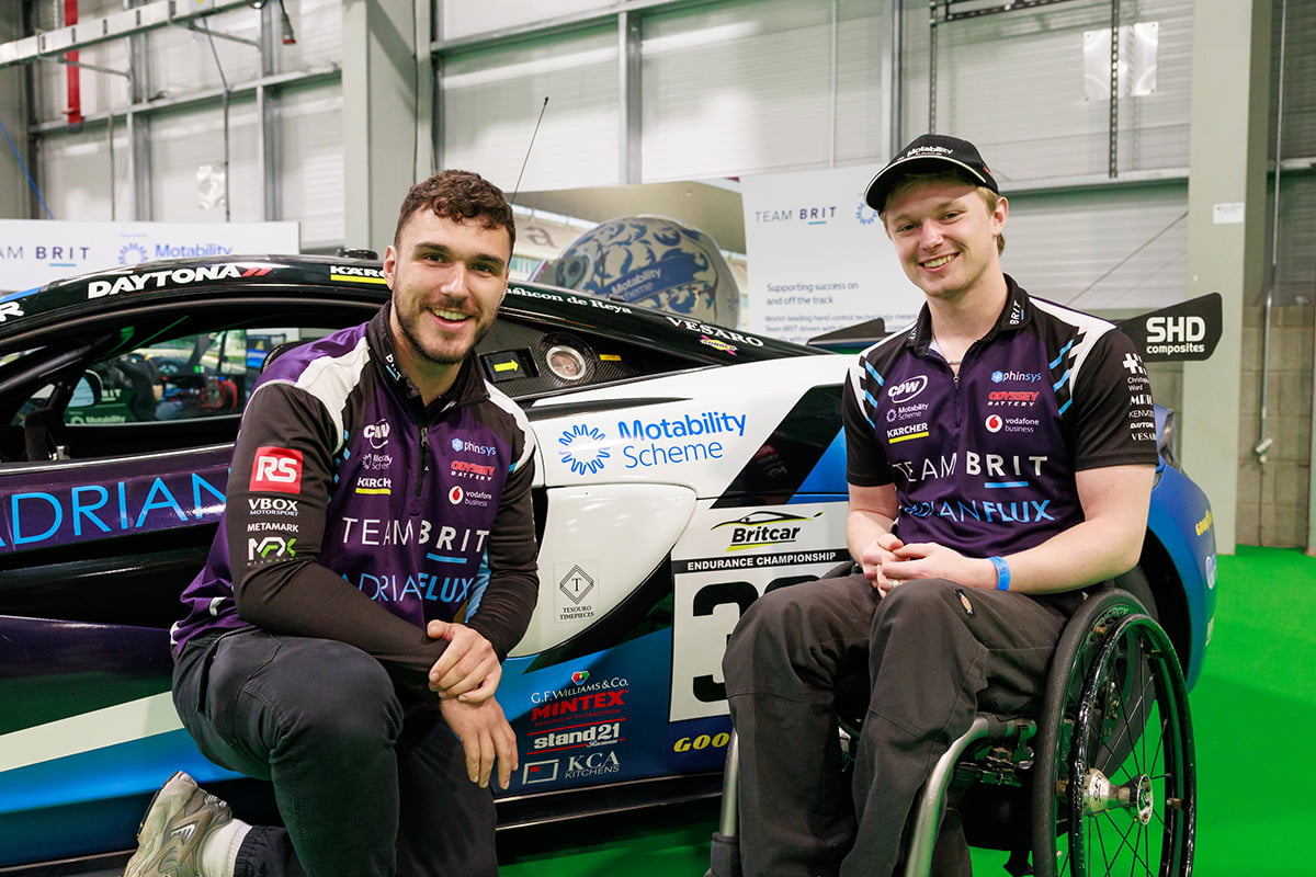 Two people in Team BRIT racing shirts posing in front of a racing car with Motability branding
