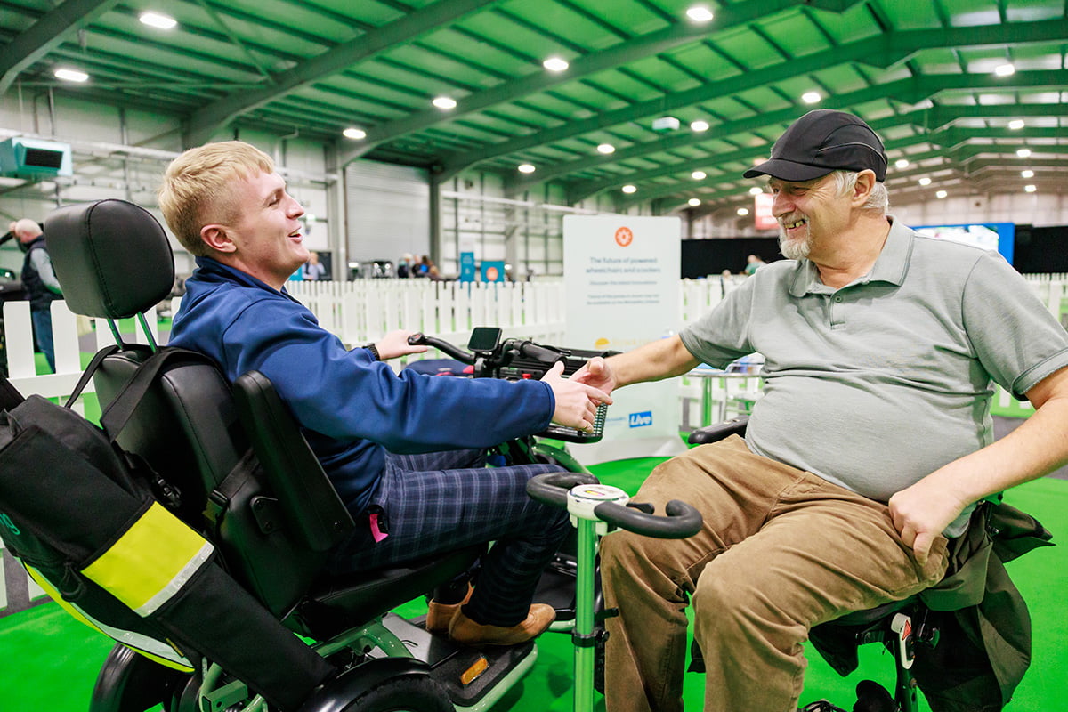 Two people in wheelchairs smiling and shaking hands